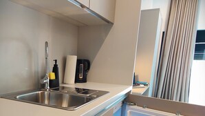 Cocina compacta con lavamanos integrado, cafetera y un mini refrigerador con bebidas.