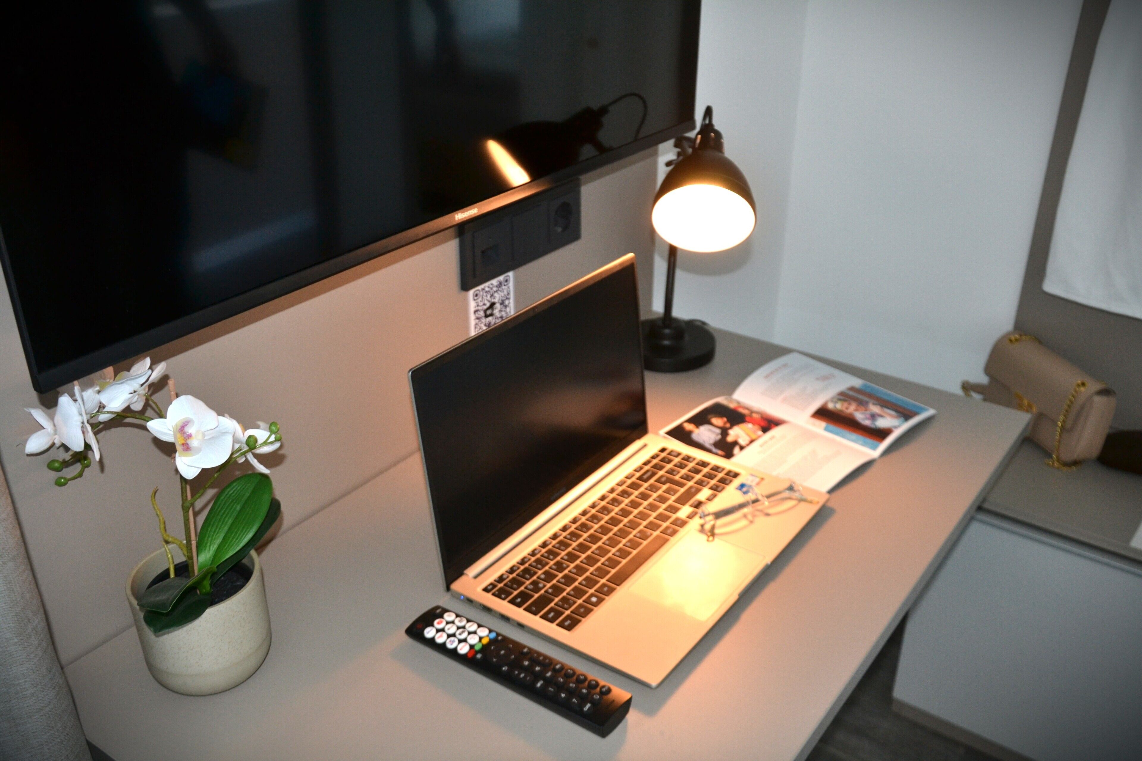 Una laptop sobre un escritorio con un control remoto, una lámpara y una planta.