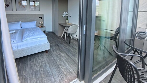 Una habitación de hotel moderna con una cama, un escritorio y un balcón con sillas.