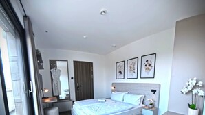 Un dormitorio moderno con una cama grande, un escritorio y una silla. Hay tres cuadros en la pared y una ventana con cortinas.