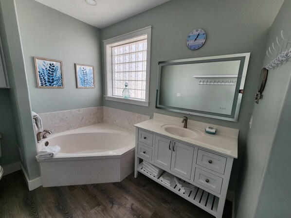 Ein Badezimmer mit einer freistehenden Badewanne, einem Waschtisch mit Spiegel und zwei gerahmten Kunstwerken an der Wand.
