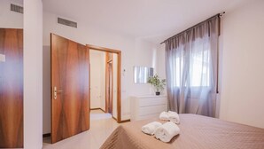 Una camera d'albergo con un letto, una cassettiera, uno specchio e una porta che dà su un'altra stanza.