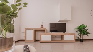 Un soggiorno moderno con una TV su un mobile in legno, un telecomando su un tavolino e due piante in vaso.