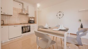 Une cuisine moderne avec des armoires blanches, un four à micro-ondes et une cuisinière. On y trouve une table à manger avec des chaises et une horloge au mur.
