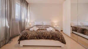 Une chambre à coucher avec un lit, deux tables de chevet, un miroir et une fenêtre avec des rideaux.