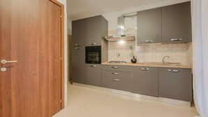 Une cuisine moderne avec des armoires grises, un four encastré, une cuisinière à gaz et une hotte en acier inoxydable.