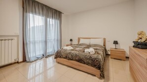 Une chambre à coucher avec un lit, deux tables de chevet, un radiateur et une fenêtre avec des rideaux.