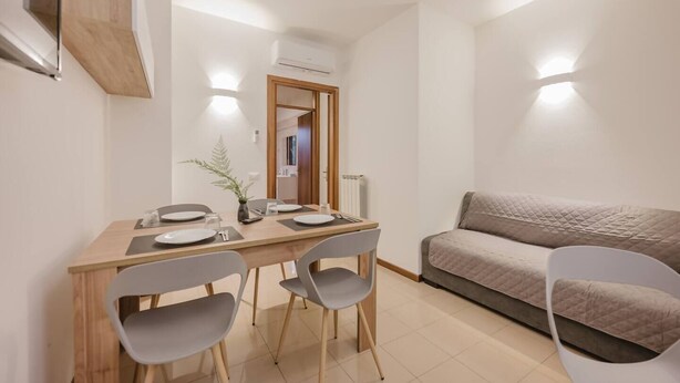Un espace repas moderne avec une table en bois et deux chaises grises, un canapé gris et une petite plante en pot.