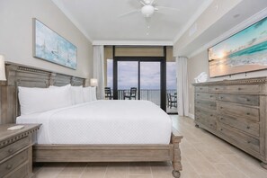 A hotel room with a large bed, a dresser, a ceiling fan, and a balcony with a view.
