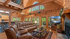 A spacious living room with a leather sectional sofa, a television, and a fireplace. - Elk Rapids On Cosby Creek 3 Bedroom Cabin (Cosby)
