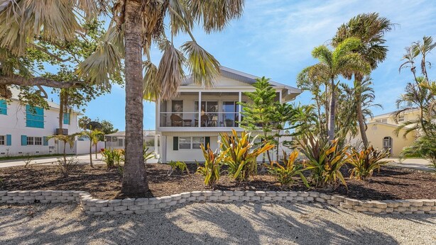 A two-story building with a balcony, surrounded by palm trees and a gravel driveway.