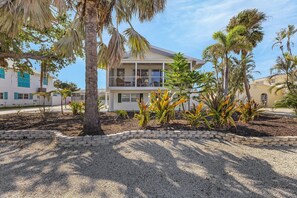 A two-story building with a balcony, surrounded by palm trees and a gravel driveway. - 140 Barefoot Bungalow: 4br/2ba W/ Heated Pool! 4 Bedroom Home (Fort Myers Beach)