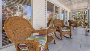 A covered patio with wicker furniture and a glass table.