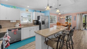 A modern kitchen with white cabinets, a stainless steel refrigerator, a built-in oven, and a bar area with bar stools.
