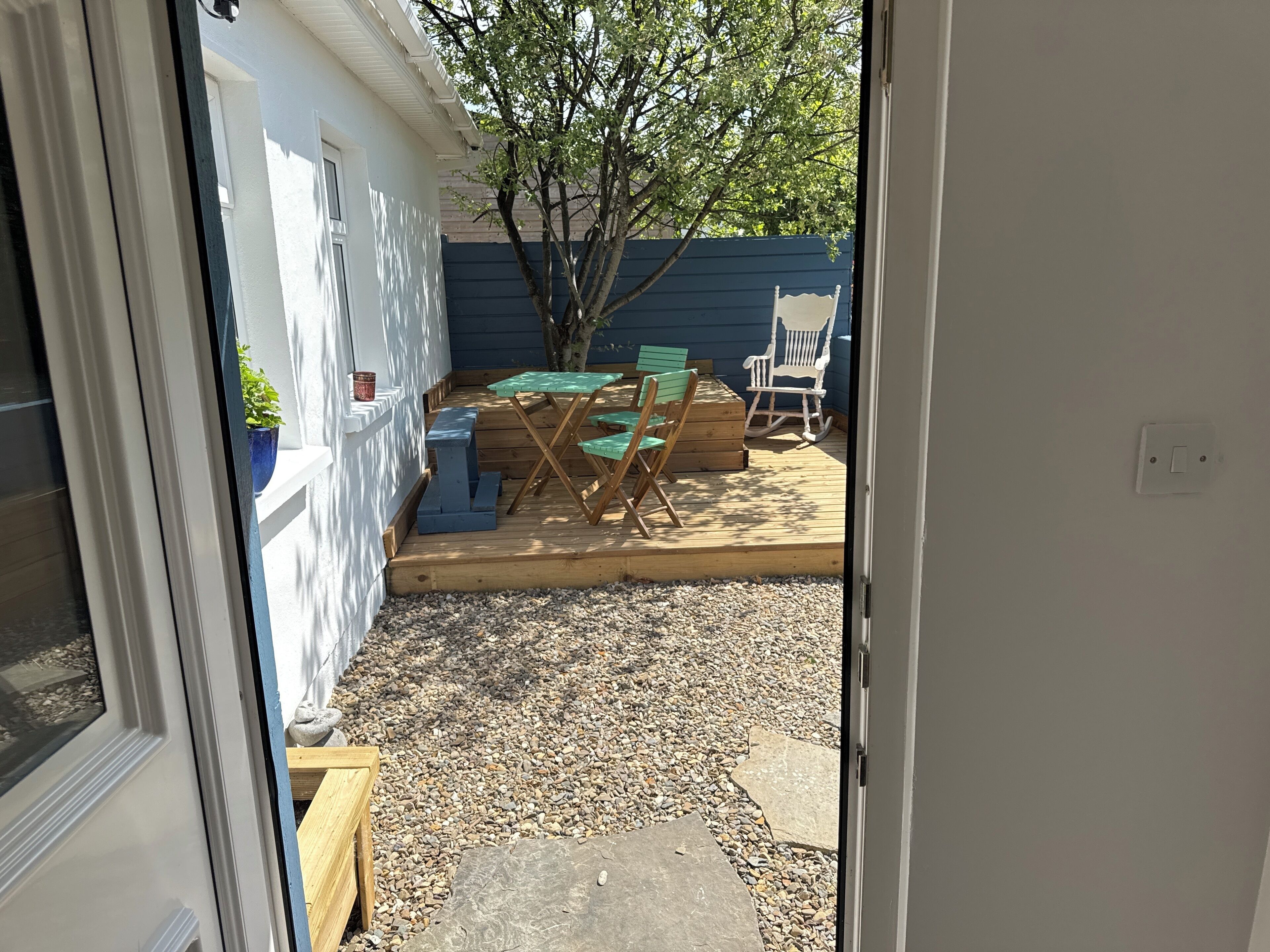 A patio with a wooden table and chairs, a rocking chair, and a small potted plant.