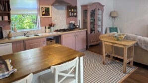 Uma cozinha com armários rosa, uma mesa de madeira e uma janela com vista para o verde.
