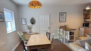 Uma área de refeições acolhedora com uma mesa e cadeiras de madeira, uma cozinha com máquina de café e um enfeite de parede decorativo.