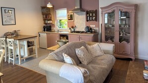 Uma sala de estar acolhedora com um sofá, uma área de refeições com mesa e cadeiras, uma cozinha com fogão e armários, e um aparador decorativo.