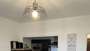 Une cuisine compacte dotée d’un îlot central, de meubles de couleur noire et d’un luminaire suspendu.