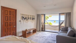 Ett sovrum med en säng, en soffa, ett TV-bord i trä och ett stort fönster med utsikt över stranden.