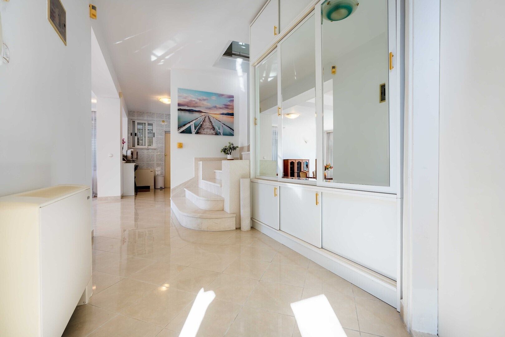 Un couloir moderne avec un escalier, une vue sur un paysage lointain et un coin cuisine.