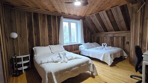 En stuga med träpanel, inredd med två sängar, ett skrivbord, en stol och ett fönster.