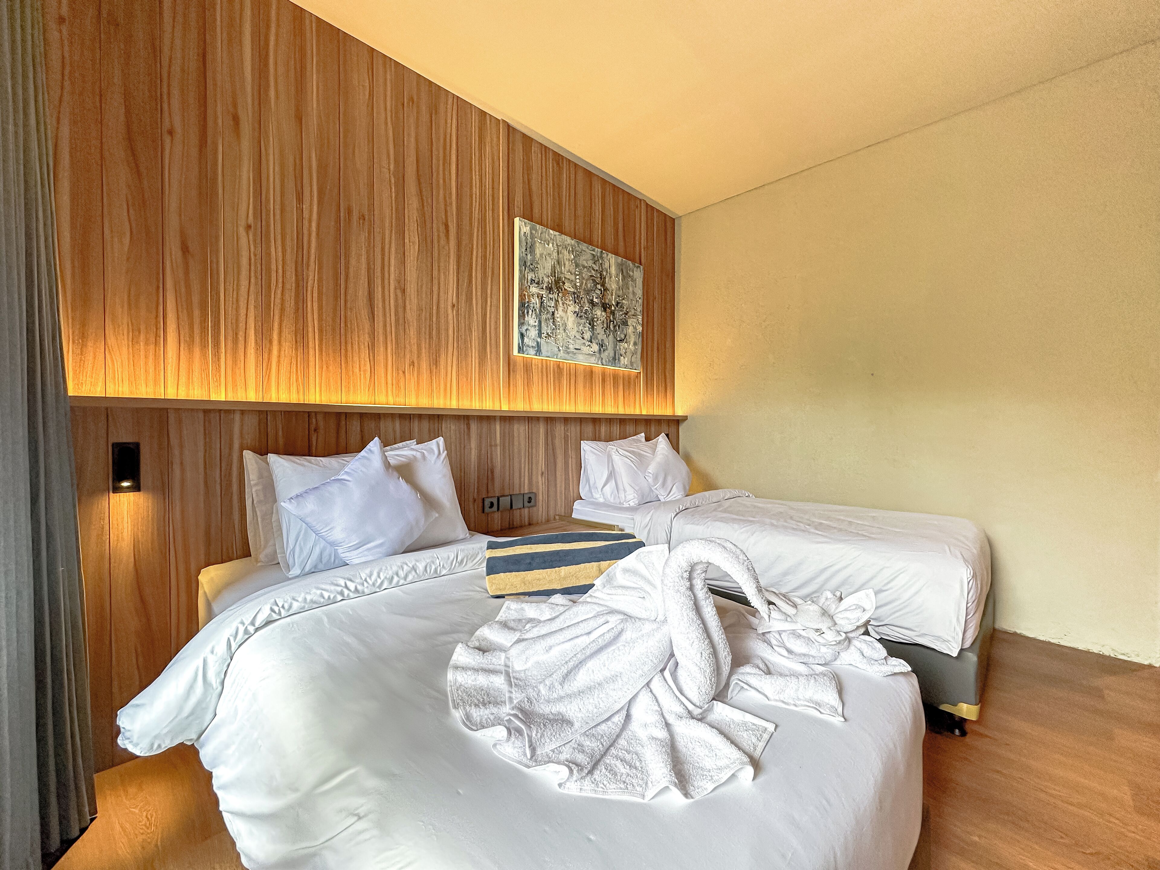 Ett modernt hotellrum med en sänggavel i trä, en stor säng med vita sängkläder och en tavla ovanför sängen.
