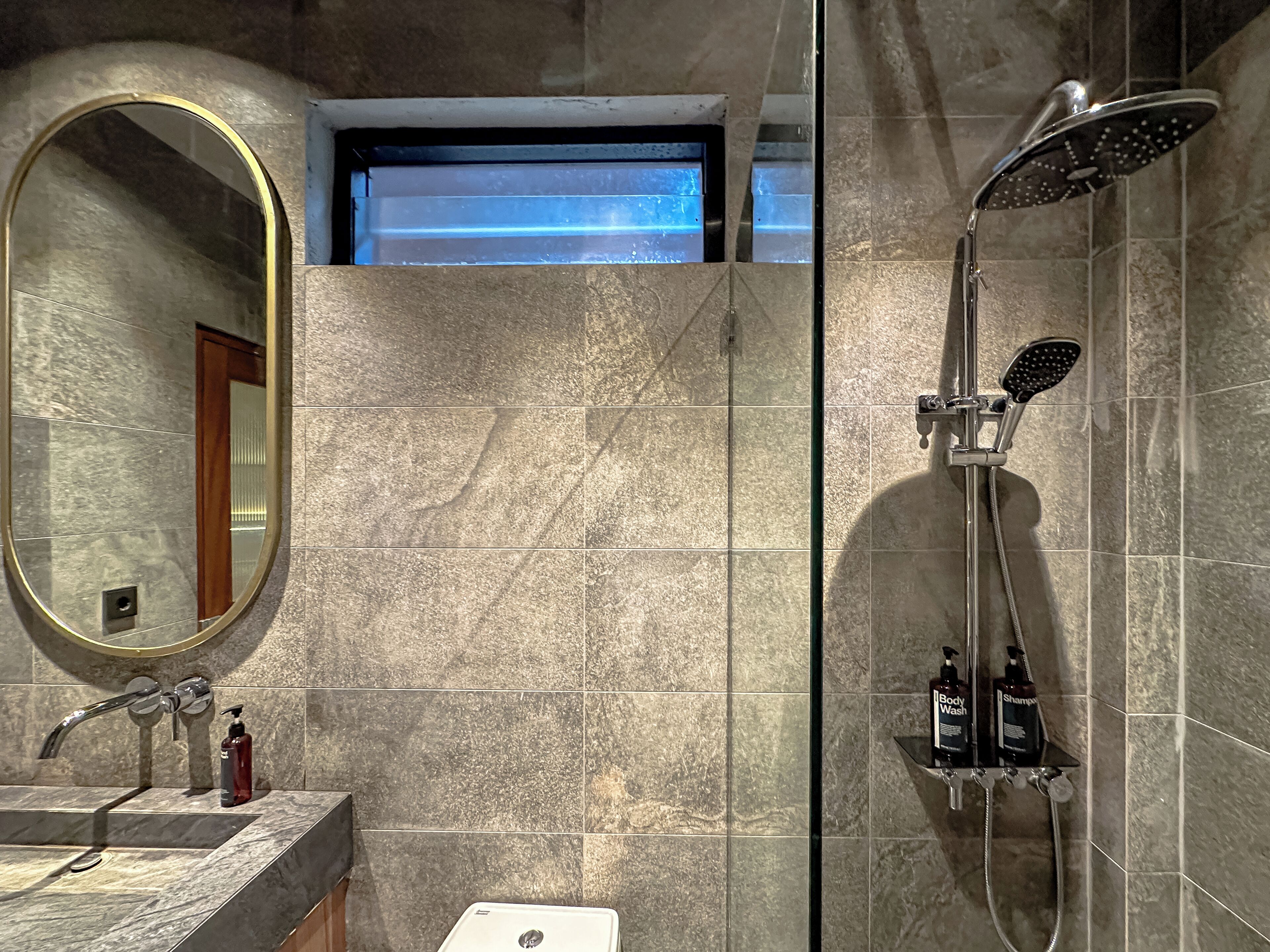 A bathroom with a large mirror, a shower with a handheld showerhead, and a sink with toiletries.
