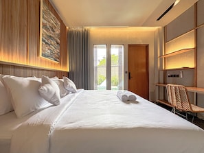 A hotel room with a large bed, a chair, a wooden door, and a view through a glass door. - Balvanta Coliving (Kerobokan)