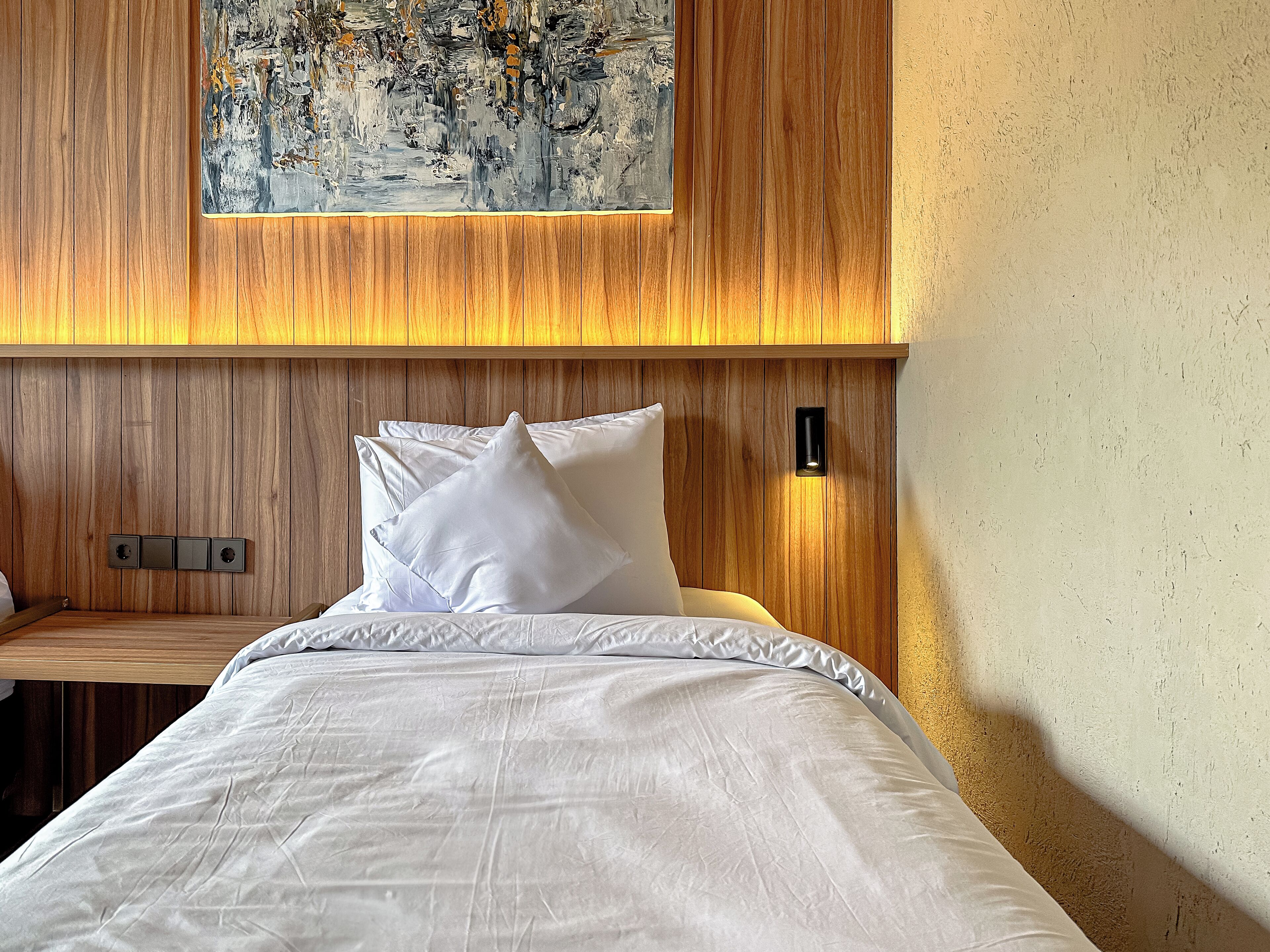 A neatly made bed with white linens and pillows, a wooden headboard, and a painting above.