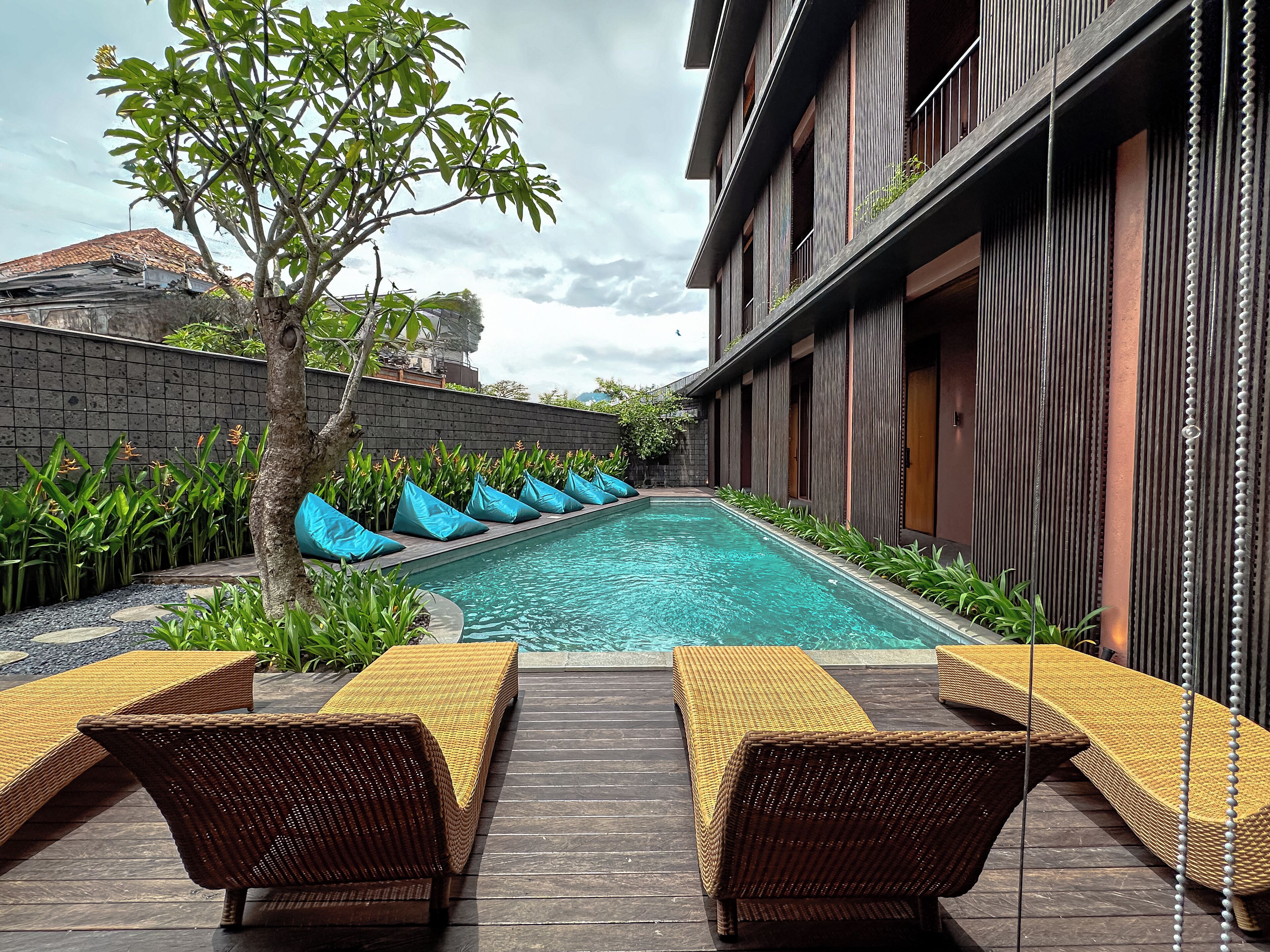 A pool area with lounge chairs, a tree, and a building with vertical wooden slats.