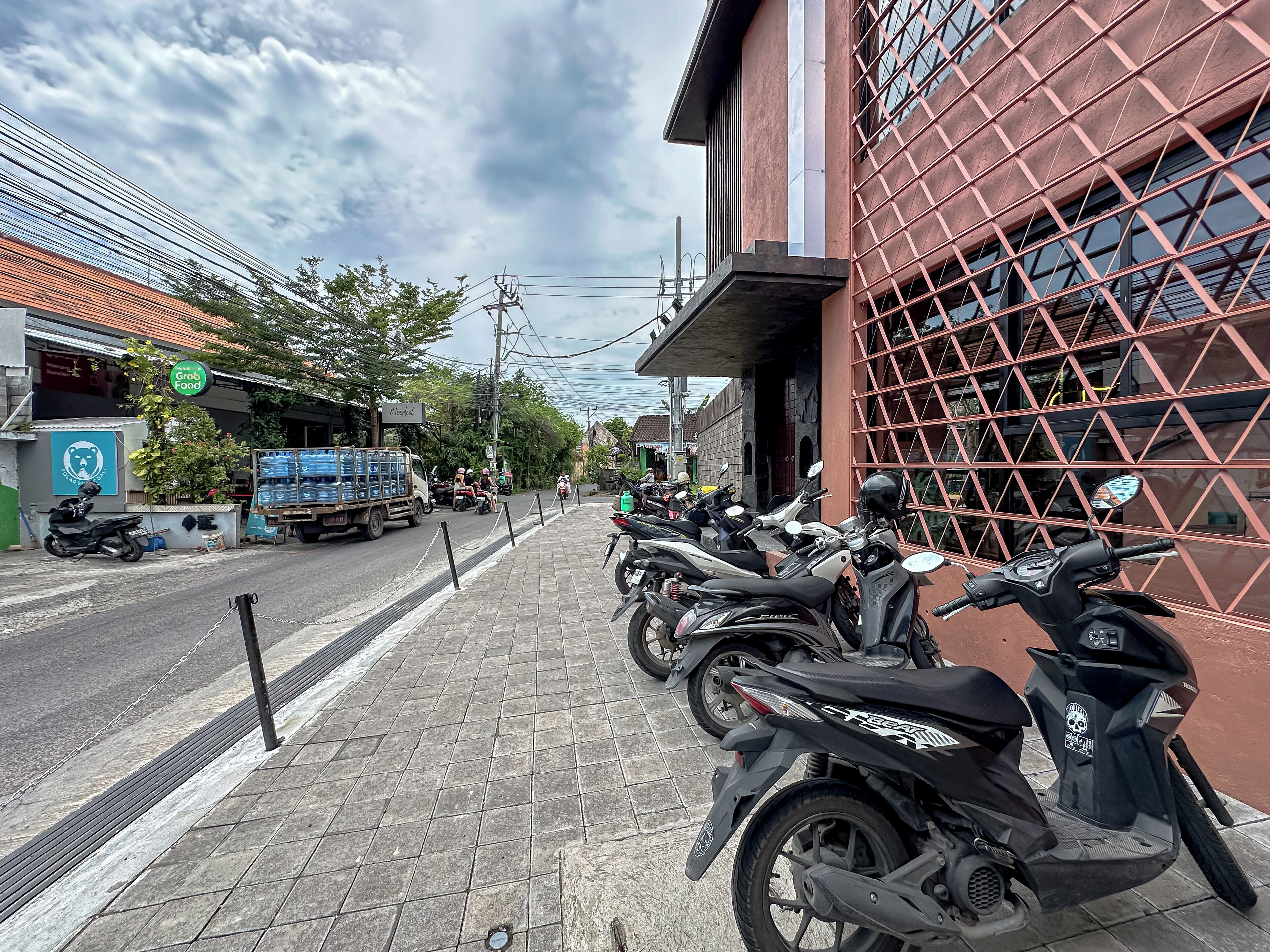 A street lined with parked scooters, a building with a red facade, and a sign for 'Grub Food'.