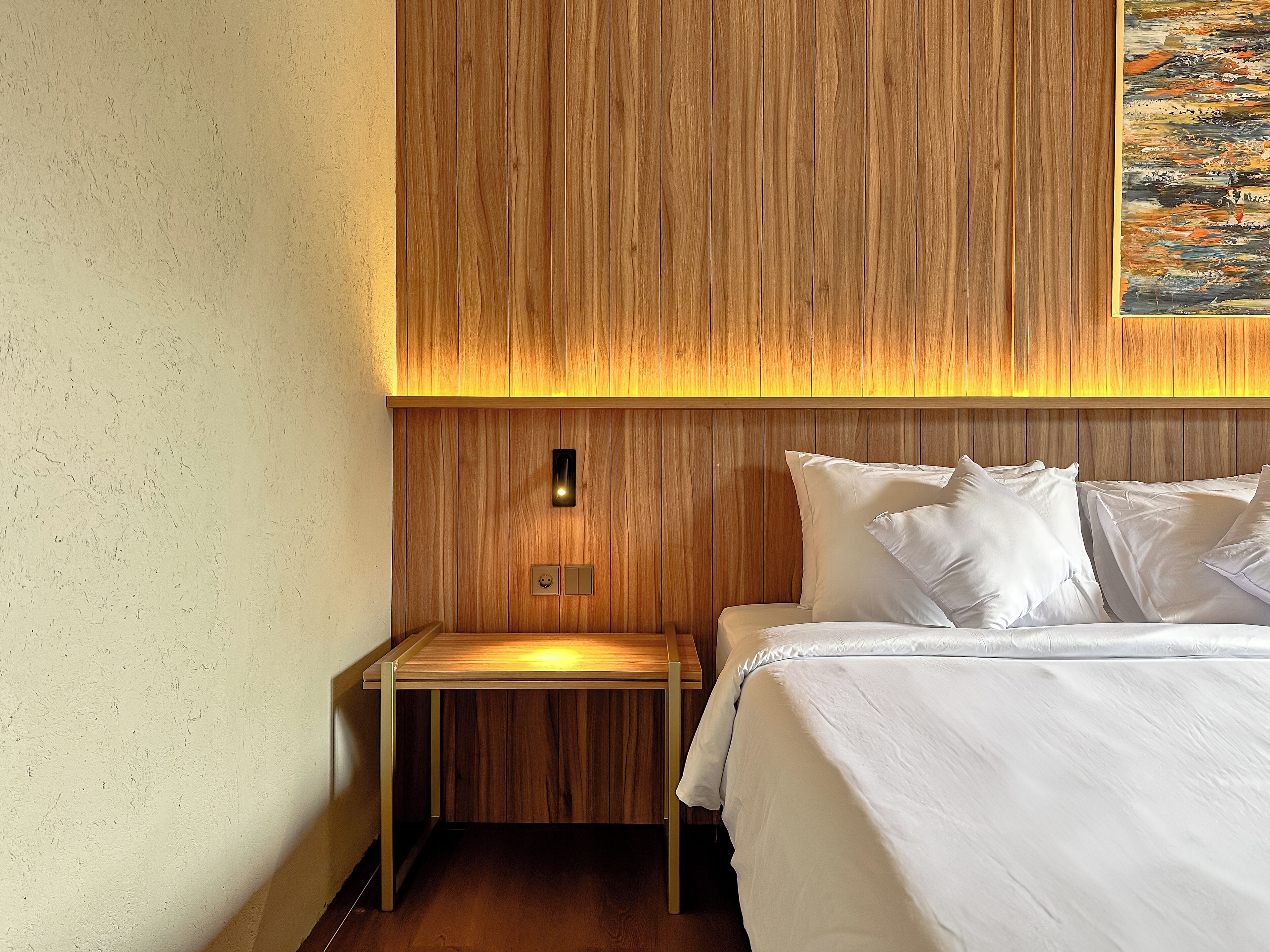 A hotel room with a wooden headboard, a bed with white linens, a nightstand, and a wall-mounted light.