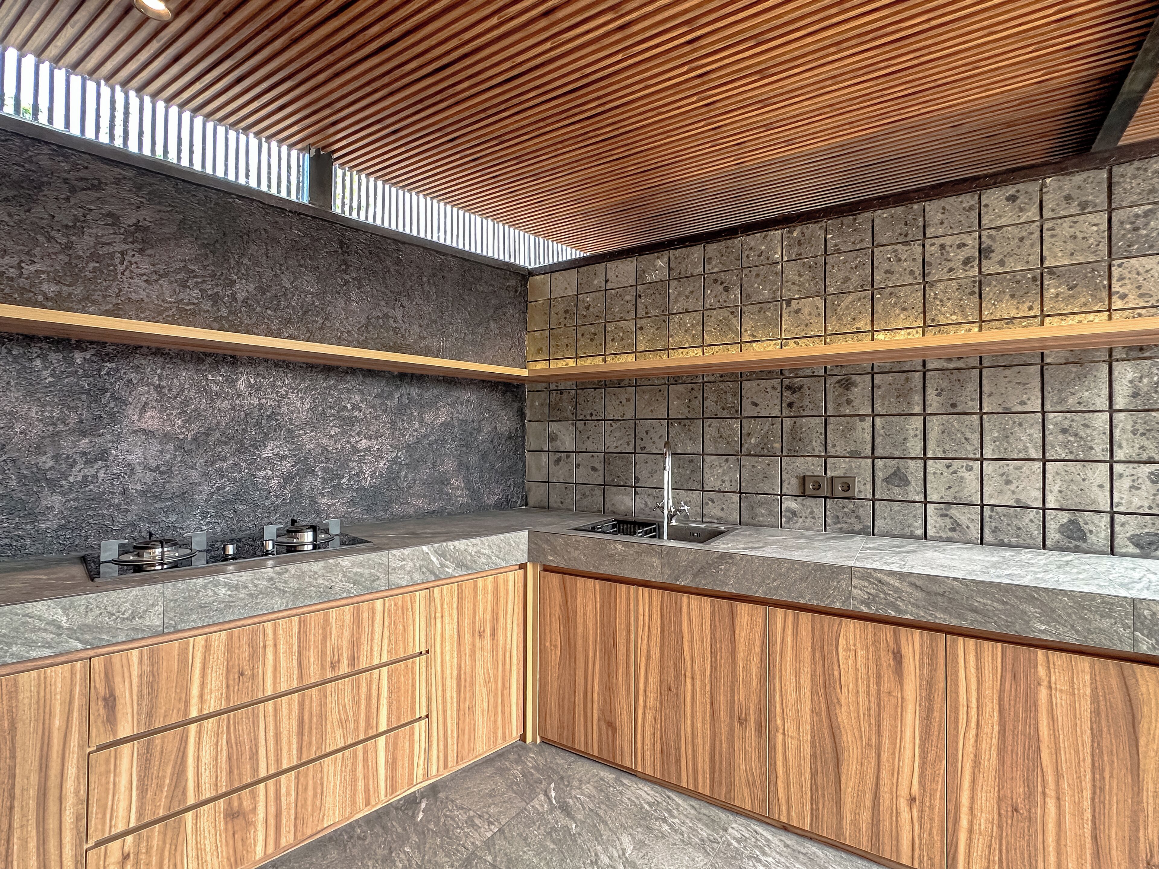 A modern kitchen with a stone backsplash, wooden cabinets, and a built-in stove.