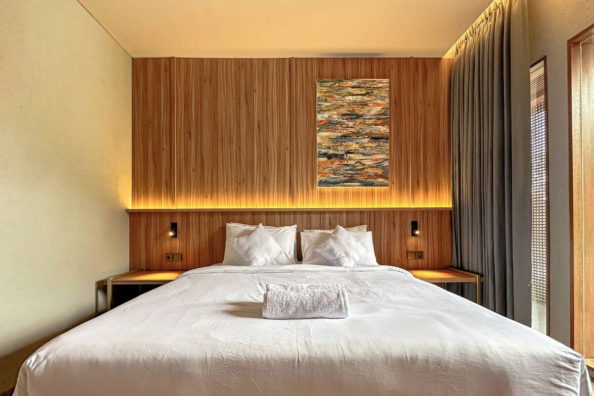 Una habitación de hotel con una cama grande, paneles de madera en las paredes, un cuadro sobre la cama y dos lámparas de noche.