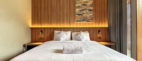 A hotel room with a large bed, wooden paneling on the walls, a painting above the bed, and two bedside lamps.