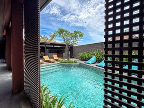 A pool area with clear water, lounge chairs, and a view of a building with a tiled roof. - Balvanta Coliving (Kerobokan)