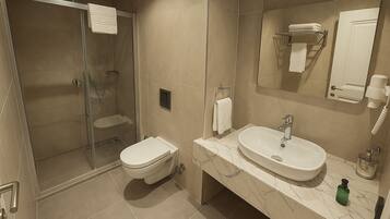 A modern bathroom with a glass-enclosed shower, a toilet, a sink with a marble countertop, and a large mirror.