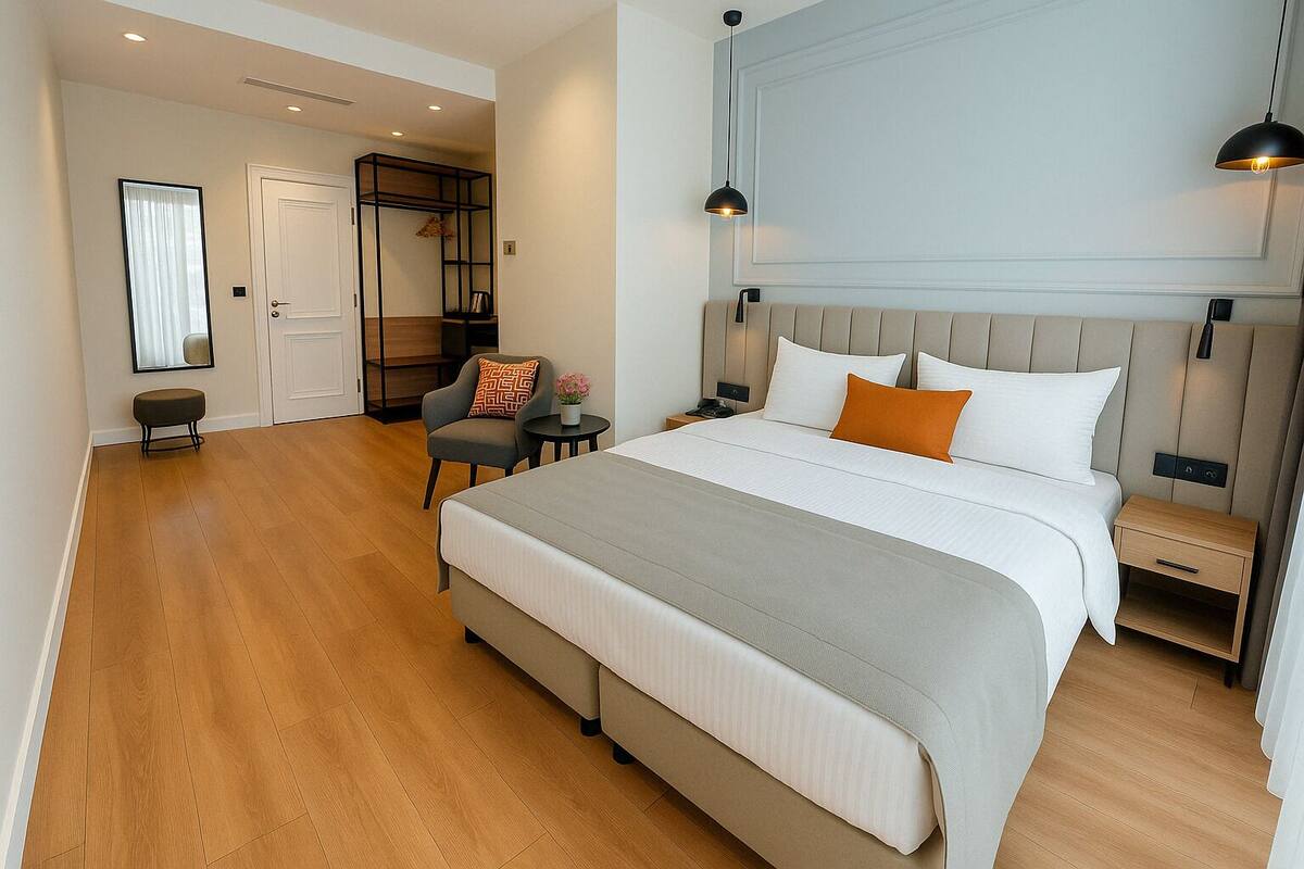 A modern hotel room with a large bed, a bedside table, a chair, a desk, and a mirror.