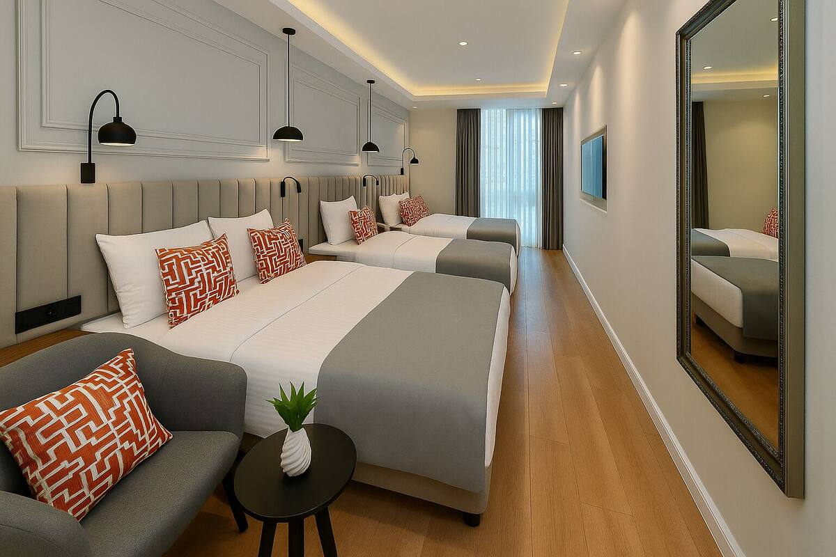 A hotel room with a large bed, a sofa, a small table with a plant, and a mirror on the wall.