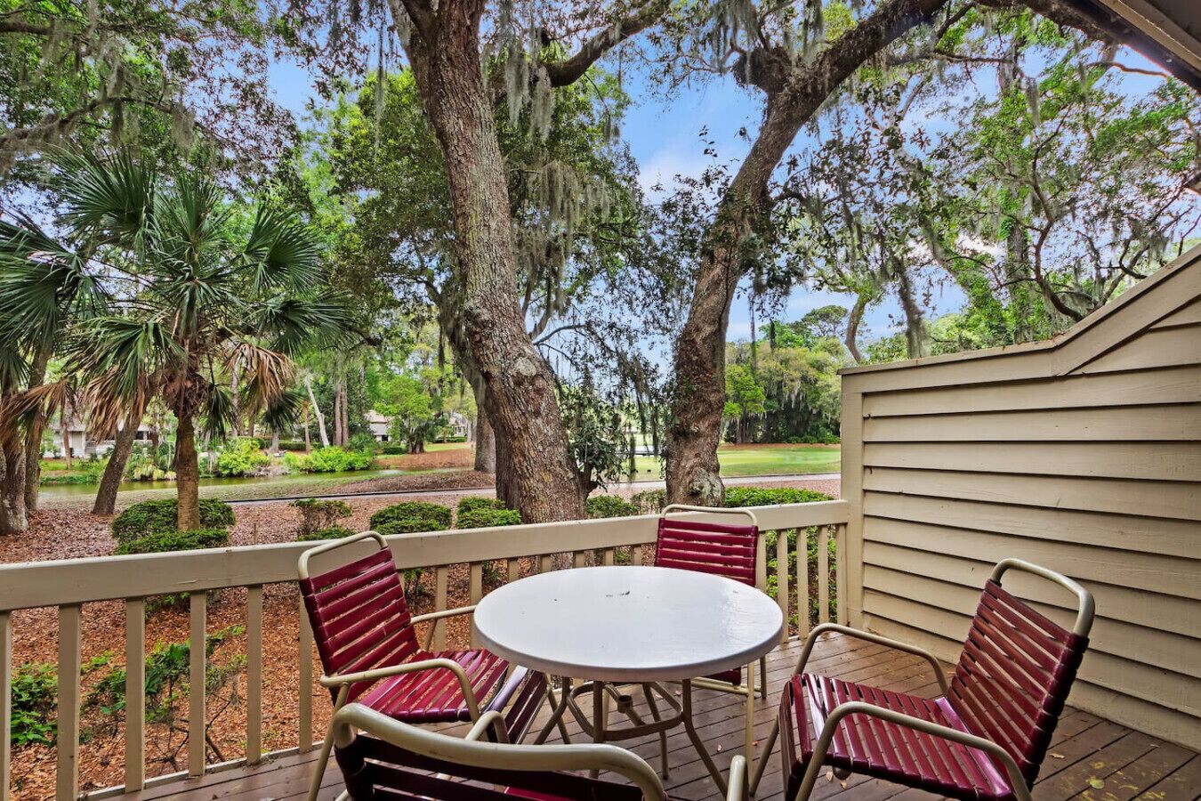 A covered patio with a round table and four chairs, surrounded by trees and a view of a golf course.
