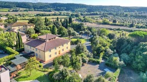 A large, single-story building with a tiled roof, surrounded by lush greenery and trees. - Resort with pool in Riparbella  (Riparbella)