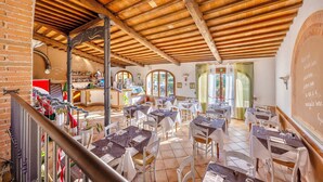 A restaurant with wooden beams and brick walls, tables set with white tablecloths and chairs, and a bar area visible in the background. - Resort with pool in Riparbella  (Riparbella)