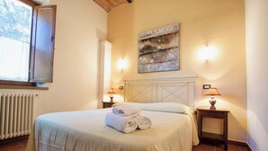 A neatly made bed with rolled towels, a radiator, two wall-mounted lamps, and a piece of abstract art on the wall. - Resort with pool in Riparbella  (Riparbella)