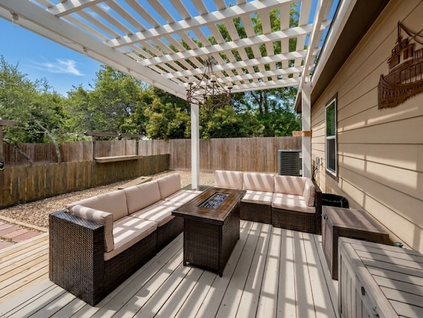 Une terrasse couverte avec un canapé d’angle, une table basse et une pergola au-dessus.