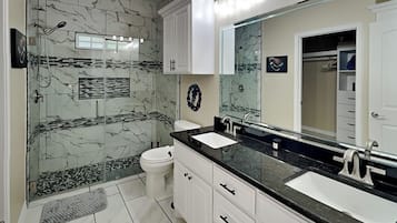 Un baño moderno con dos lavamanos, cabina de ducha de cristal y un espejo grande.