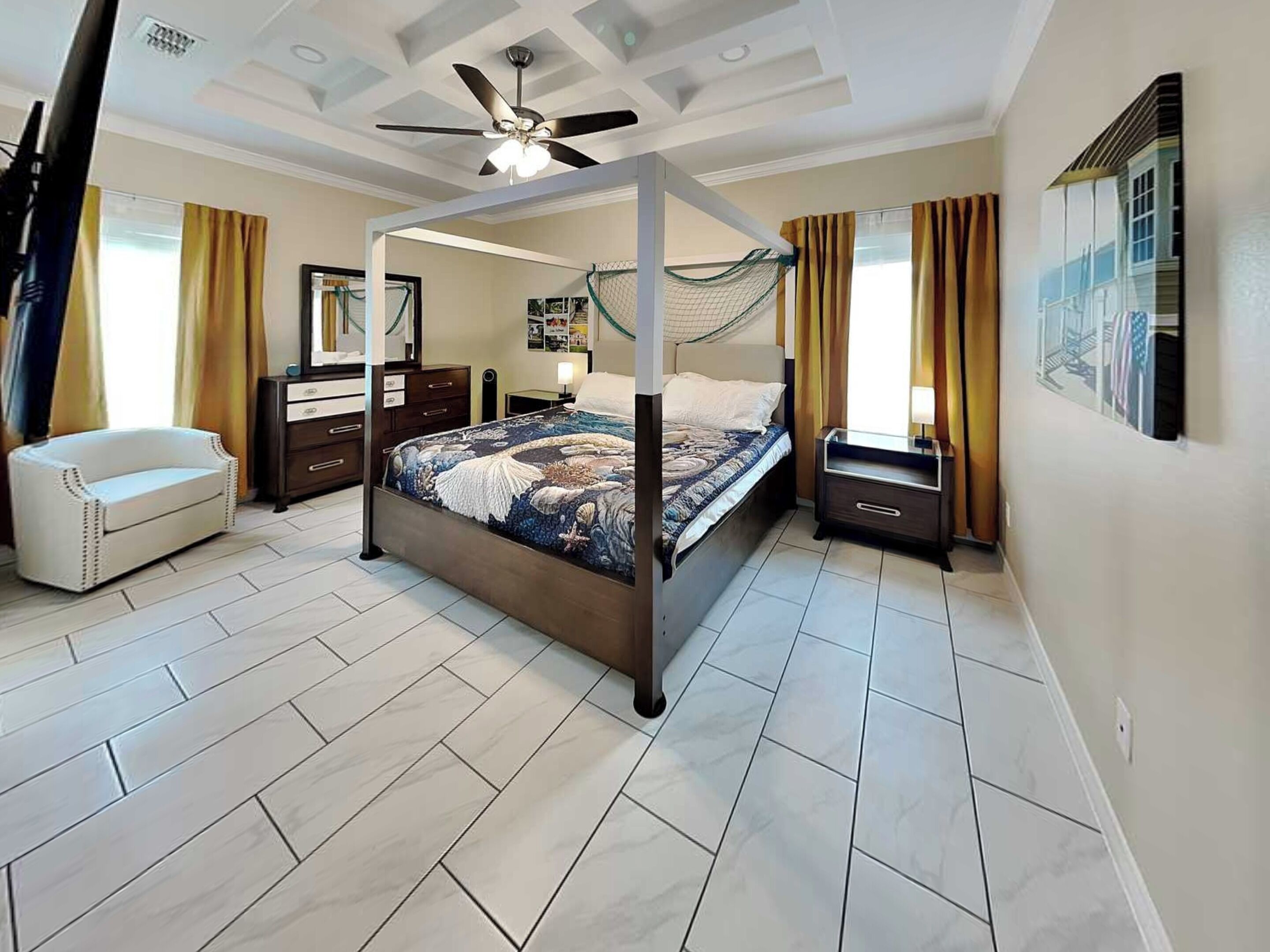 A bedroom with a four-poster bed, a ceiling fan, a nightstand, a dresser, and a chair.