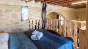 Ein rustikaler Raum mit Steinwand, Holzbalkendecke, einem Bett mit blauer Bettdecke und einem Holzbalken.