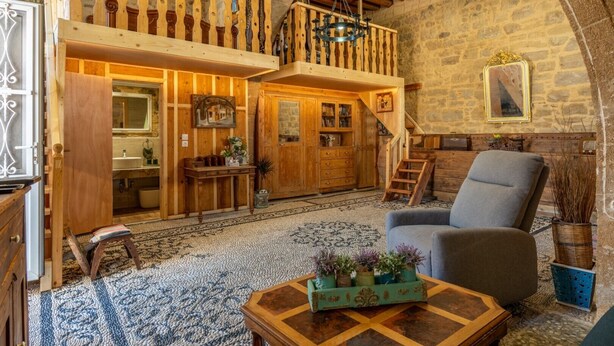 Ein rustikaler Innenraum mit einer Holztreppe, einem Balkon, einer Essecke und einer Sitzecke mit Stuhl und Tisch.