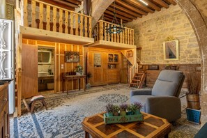 A rustic interior with a wooden staircase, a balcony, a dining area, and a seating area with a chair and a table.
